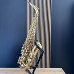 Shiny gold saxophone resting on a black stand in a music studio with a blue wall and wooden panel background.
