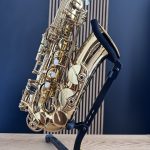 Close-up of a gold saxophone resting on a black stand against a blue wall.