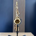 Gold saxophone on a stand against a blue wall with striped paneling, viewed from above in a music studio.