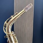 Close-up of a gleaming brass saxophone neck with keys, against a blue background.