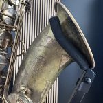Close-up of a worn brass musical instrument with valves, tubing, and engravings visible on the body.