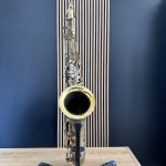 Saxophone on a stand against a blue wall with vertical striped panels in the background, upright and ready for display of the instrument
