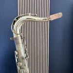 Close-up of an antique brass saxophone neck with cork mouthpiece against a dark blue background.