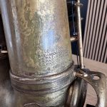 Close-up of a worn metal surface with engraved text, including 'MADE IN FRANCE' and 'US PAT' markings, showing corrosion and a threaded base.