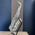 Gold saxophone resting on a black stand against a blue wall, angled diagonally across the frame.