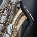 Close-up of shiny saxophone keys and rods resting on a wooden surface with a black strap nearby.