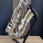 Close-up of a shiny brass saxophone resting on a stand, showing keys, rods, and bell against a dark blue background.