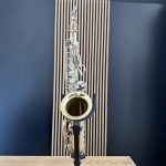 A brass saxophone on a stand in a rehearsal room with blue walls and vertical wood slats behind it.