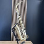 Brass saxophone resting on a black stand in a studio with blue walls and vertical wooden slats behind it.