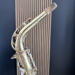 Close-up of a tarnished brass saxophone neck with cork, set against a dark background.
