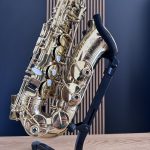 Close-up of a gold saxophone on a black stand against a blue backdrop.