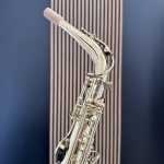 Close-up of a silver saxophone neck with mouthpiece and cork, against a blue background with vertical lines.