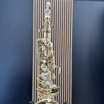 Close-up of a silver saxophone neck and mouthpiece against a blue background.