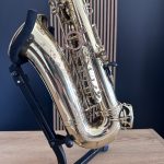 Close-up of a shiny brass saxophone on a black stand, highlighting keys and rods against a dark blue backdrop on a wooden surface.