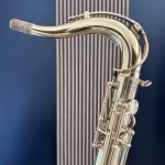 Close-up of a polished brass horn with curling tubing and a light-colored mouthpiece against a blue wall.