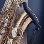 Close-up of a gold brass saxophone showing its shiny keys, rods, and body laid on a wooden surface with a dark blue background.