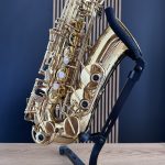 Close-up of a gold brass saxophone resting on a black stand against a blue wall.