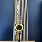 Gold saxophone on a black stand against a blue wall with a vertical striped backdrop. (Informative)