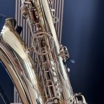 Close-up of a shiny brass saxophone showing keys, rods, and curved body against a dark background